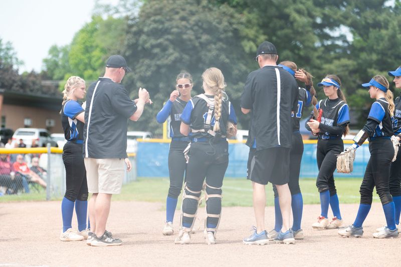 Harper Creek players and coaching staff huddle up between innings during a game against Coldwater at Harper Creek High School on Saturday, May 31, 2025.