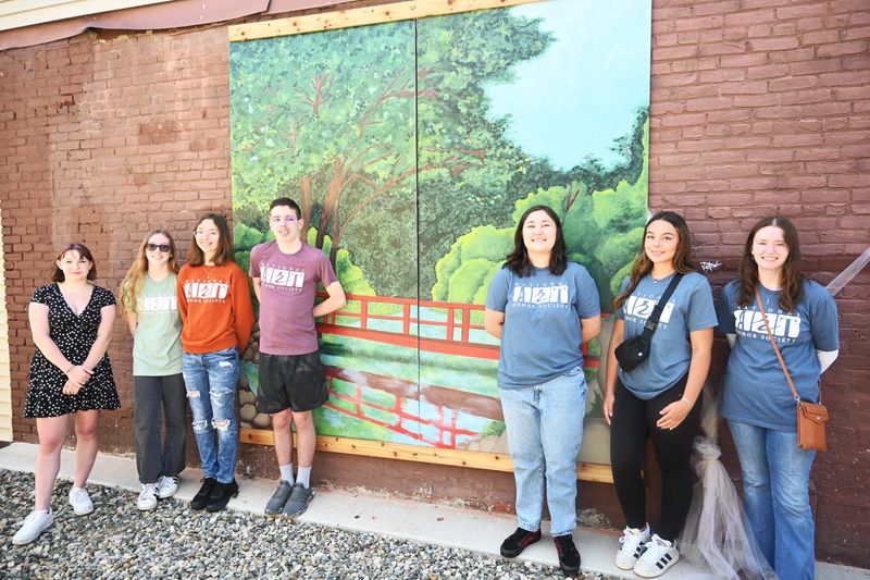 Coldwater students Gracelyn West, Kaitlyn Coger, Ashlyn Caswell, Landon Baker, Lily Thomas, Carly  Krazyanski, and Allie Miller stand before the mural showing the bridge over the Sauk River in Waterworks Park.