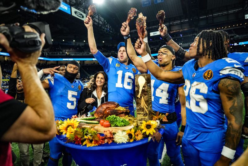 Detroit Lions quarterback Jared Goff (16), defensive tackle DJ Reader (98), wide receiver Amon-Ra St. Brown (14), running back Jahmyr Gibbs (26), linebacker Al-Quadin Muhammad (69) celebrate their win against the Chicago Bears with a turkey drumstick after winning 23-20 on Thanksgiving Day at Ford Field in Detroit on Thursday, Nov. 28, 2024.