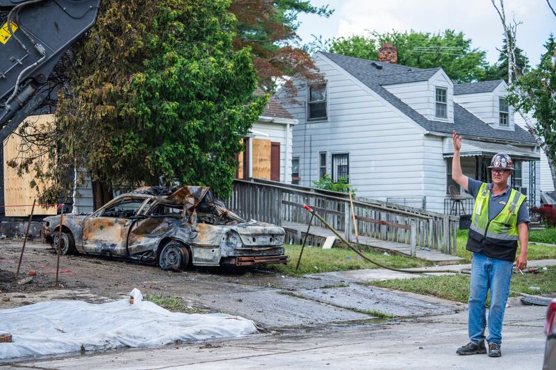 A workers signals to a tow truck to remove a destroyed car in the remnants of a home explosion that left one dead and one injured on McCormick Street off of Moross Road in Detroit on Sunday, July 6, 2025. The explosion damaged two neighboring homes, and neighbors said they felt the explosion blocks away.