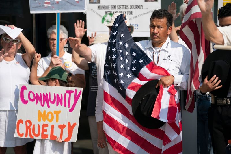 Miguel Leyva, of Rochester, holds an American flag as he and son join a group of Catholics and others who support immigrants “Strangers No Longer” walk from the historic Most Holy Trinity Catholic Church in Corktown on Monday, July 14, 2025 to deliver a letter to the Detroit ICE regional field office director Kevin Raycraft, asking for individuals be treated with dignity. Hundreds prayed during the protest for family and community members who have recently been detained or deported by ICE.