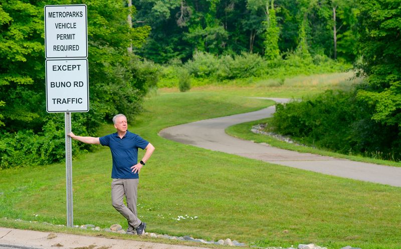 Bill Huszti stands at signage on Huron River Parkway just off West Buno Road in Milford on Wednesday, July 16, 2025. He lives on West Buno Road, an unofficial free entrance into Kensington Metropark.