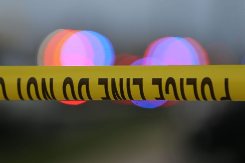 Police tape is strung up with police sirens flashing in the background.

Police tape