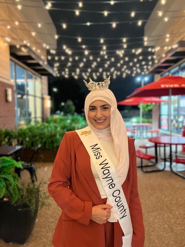 Miss Wayne County 2025 Ameera Hashwi, of Dearborn Heights, outside Qahwah House, a cafe, in Dearborn Heights in August 2025, wearing her crown and sash. The 25-year-old attorney is the first winner of Miss Wayne County to wear an Islamic headscarf, known as hijab.