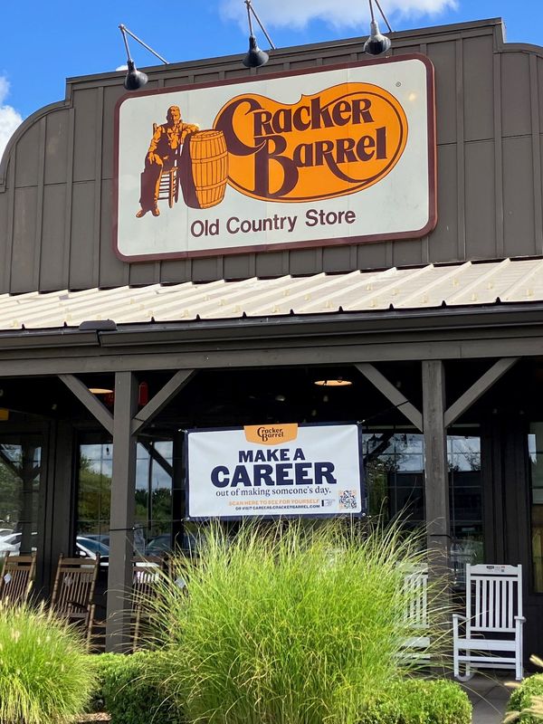 A help wanted banner bearing Cracker Barrel’s new logo flies beneath the old logo Tuesday, Aug. 26,2025, at the restaurant in Belleville. Later in the day, the company announced that it was reversing its decision and would keep the logo with the barrel and the man in overalls.