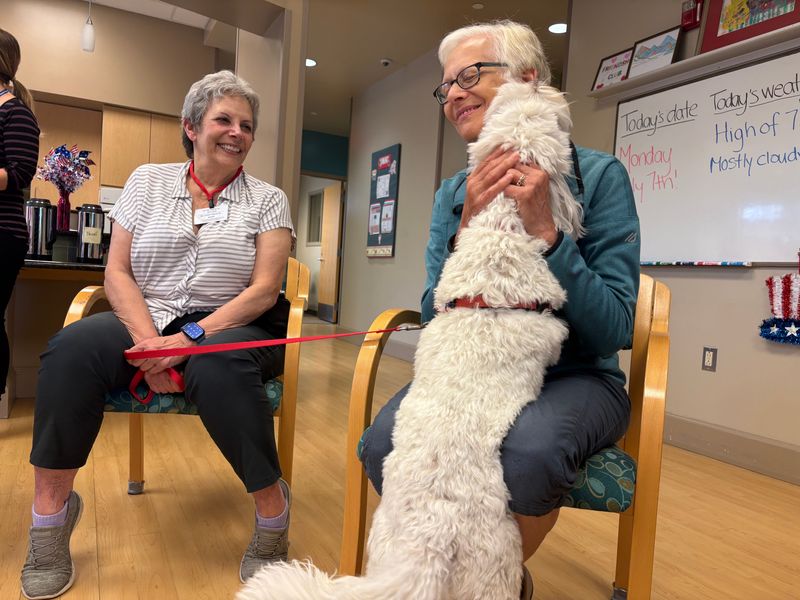 Kay Presby, right, holds Raffi, an Australian labradoodle, at the Friendship Club, which is Bloomfield Township's adult day service, on July 7, 2025. Presby is joined by Teryl Asher, left.