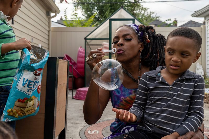 Lorna Parks, 57, founder of House of Joy Child Care, blows a large bubble as Braelyn Parks, 6, sits in her lap during an activity in the backyard of her home in Detroit on Friday, Sept. 19, 2025.