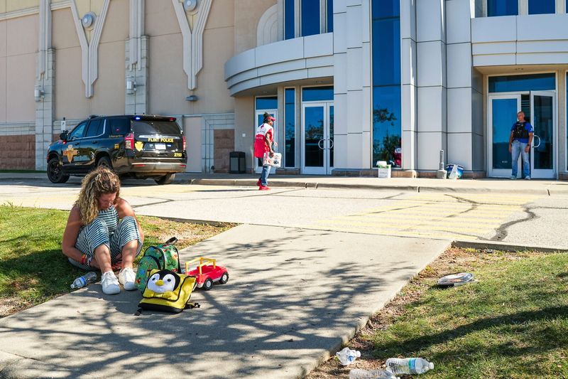 A person sits outside of NCG Trillium Cinema, which is acting as a reunification center, following a shooting and a fire at the Church of Jesus Christ of Latter-day Saints in Grand Blanc on Sunday, Sept. 28, 2025.