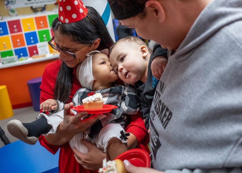Michigan State University pediatrician professor Dr. Mona Hanna-Attisha, left, reacts as Emani Loveé, 11 months, of Flint, kisses the head of Braylon Brooks, 1, as he leans into her while being held by his mother Melissa Brooks, 41, of Flint, while eating cupcakes during a 1-year anniversary party for the Flint Rx Kids cash assistance program in Michigan at the Flint Children’s Museum in Flint on Wednesday, Jan. 29, 2025. The program received $20 million in federal dollars to expand beyond Flint, where it began.