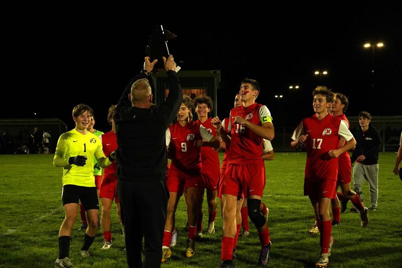 New Boston Huron boys soccer coach Matt Lividini presents the trophy to his players after an 8-0 Huron win in the finals of the Division 2 District at Adrian on Thursday, Oct. 16, 2025.