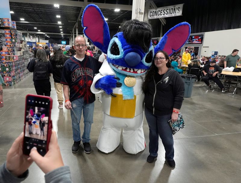 Left to right: Josh Gregory, 50, and Elizabeth Moore, 45, both from Taylor, have their picture taken with Stitch from Disney's "Lilo & Stitch." Stitch was dressed as Elvis during Motor City Comic Con at the Suburban Collection Showplace in Novi on Saturday, Nov. 15, 2025.
