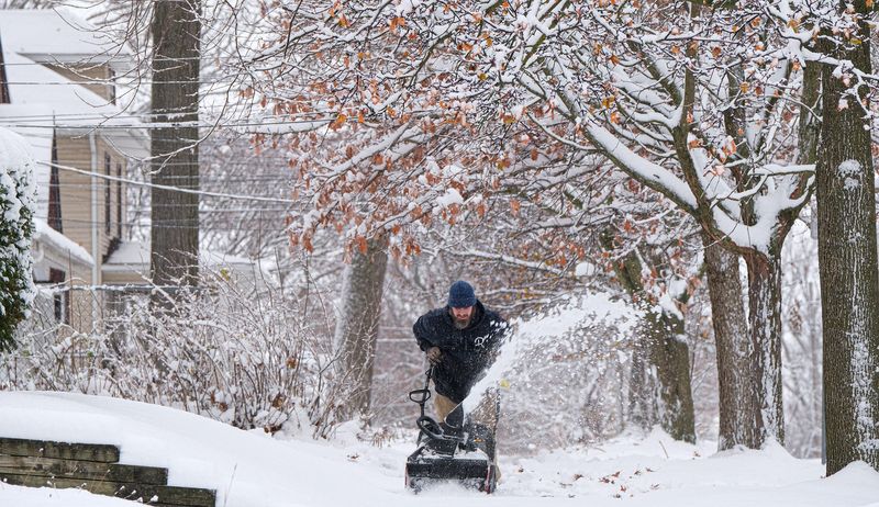 Justin Johnson leans into his snow blower as he works to clear the sidewalk of several of his Lansing neighbors, after an overnight storm blanketed the area with over five inches of heavy snow Sunday, Nov. 30, 2025.