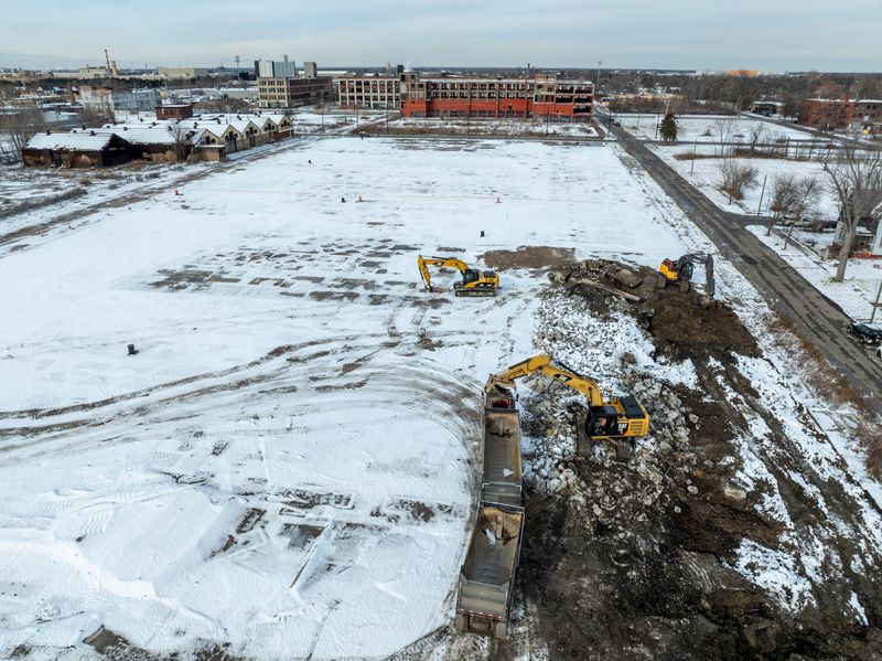 Heavy equipment operators remove concrete from an otherwise empty field as work begins on the 28-acre Packard Park redevelopment plan, on the site of the former Packard Plant. A section of the former Packard Plant building along East Grand Boulevard (top), will be renovated and preserved, becoming the most prominent building in the development. Photo taken on Monday, Dec. 1, 2025. A plan to redevelop a 28-acre portion of the Packard Plant site includes a new 400,000-square-foot manufacturing building and adaptive reuse of an existing Packard Plant building south of Grand Boulevard for an indoor skate park, 42 affordable housing units, and an electronic music museum. The former Packard Plant had stood vacant for roughly 60 years before the City of Detroit razed unsalvageable portions of the century-old manufacturing complex to create new development opportunities.