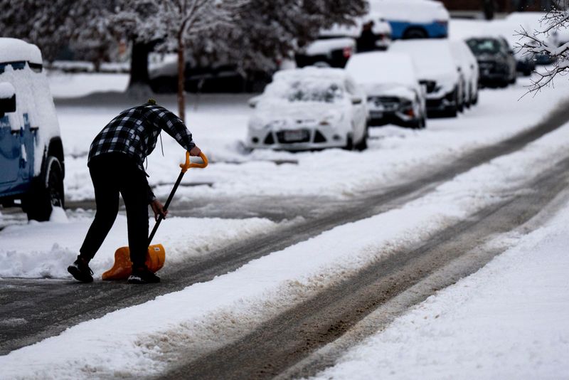 A pedestrian clears snow from the road in West Price Hill on Dec. 2, 2025.