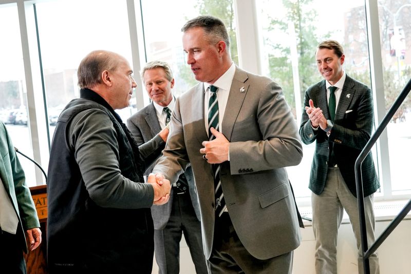 Michigan State football coach Pat Fitzgerald, right, shakes hands with Greg Williams, left, during Fitzgerald's introductory press conference on Tuesday, Dec. 2, 2025, at the Tom Izzo Football Building in East Lansing.