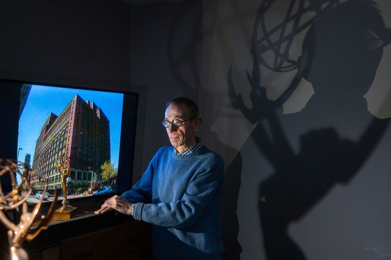 Filmmaker Gary Glaser, 75, of Farmington Hills, stands next to a frame grab from one of his documentaries on the Hudson’s building in a room of his home on Thursday, Jan. 29, 2026. Nearby are a couple of his Michigan Emmy awards. Glaser’s film includes one-of-a-kind interviews with the woman who invented the famous Hudson’s Maurice salad, and Namon Clarke, the elevator supervisor who was the store’s first Black man in a position of authority. He is trying to sell the rights to his work — partly because he needs the money, but also because should he die, his work will disappear for 70 years because of copyright laws.