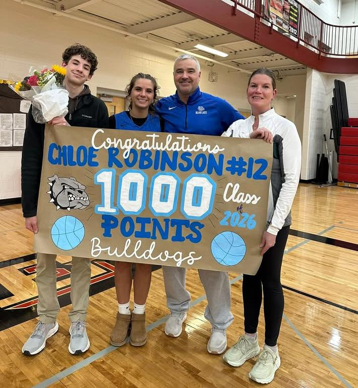 With family by her side, Inland Lakes senior Chloe Robinson holds up a sign that honored her for scoring 1,000 career points during a game at Bellaire last week.
