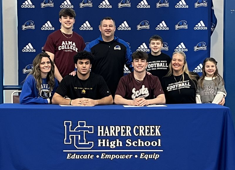Harper Creek seniors (center, from left) Kowen Slucter and Cameron Converse, committed to play football at the college level during a signing ceremony at Harper Creek High School. Slucter is planning to attend Adrian College and Converse is going to Alma College are joined in the photo by their families.