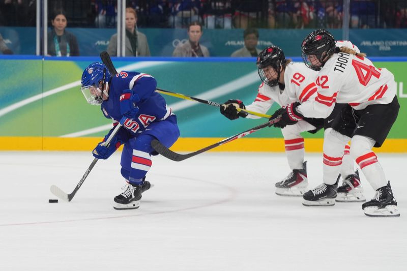 Cayla Barnes (3) of the United States controls the puck in front of Brianne Jenner (19) of Canada and Claire Thompson (42) of Canada in the women's ice hockey gold medal game during the Milano Cortina 2026 Olympic Winter Games at Milano Santagiulia Ice Hockey Arena in Milan on Thursday, Feb. 19, 2026.