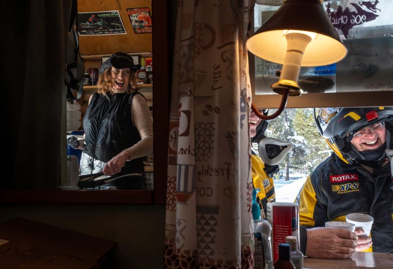 Chic Drozdrowski, 57, of Paradise, talks with Mike Hubbs, center, of Thetford Township, and his brother-in-law Todd Tindall, of Lapeer Township, as she cooks their hot dog and brat order on Thursday, Feb. 12, 2026.