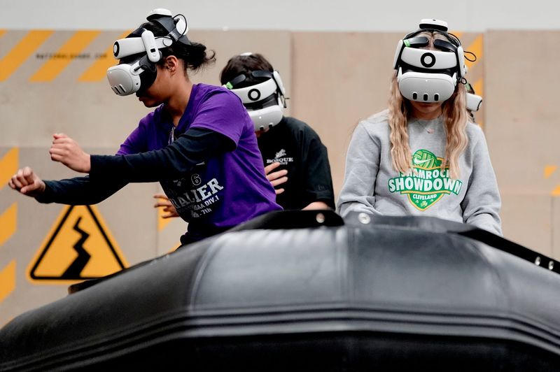 Woodhaven High School freshman Kelli Gish, 14, left, and Payton Koski, 15, pretend to paddle in a virtual flooding simulation during a program run by the Army National Guard in the school’s auxiliary gym on Friday, March 6, 2026.