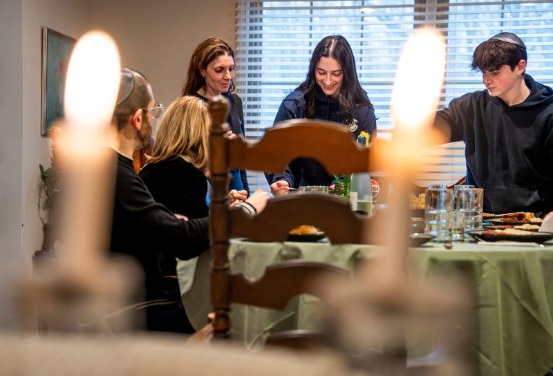 Leslie Katz, left, of Farmington Hills, waits for her daughter Ariella Katz, center, and son, Eli Katz, right, to get their food from a dish while hosting a weekly Shabbat dinner at Katz’s home in Farmington Hills on Friday, March 13, 2026.