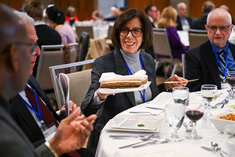 Nancy Bluth of Bloomfield Township passes a plate of matzah bread to other diners at her table during a Global Diplomatic Interfaith Seder at Adat Shalom Synagogue on Tuesday, March 24, 2026 in Farmington Hills, Mich.