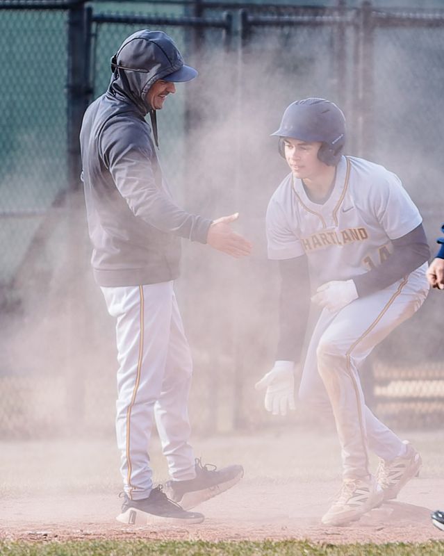 Hartland's Michael Bernardi, who was 2-for-3 with four RBIs, celebrates a triple with coach Brad Guenther during a 9-3 victory over Howell Tuesday, March 24, 2026.