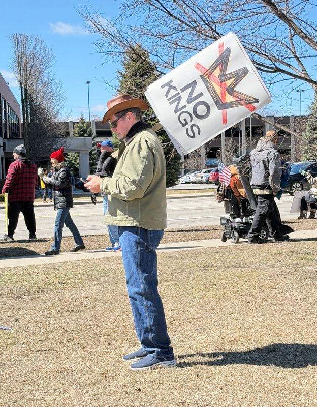 A protester holds a “No Kings” sign along Pine Grove Avenue during a demonstration in Port Huron on March 28, 2026.