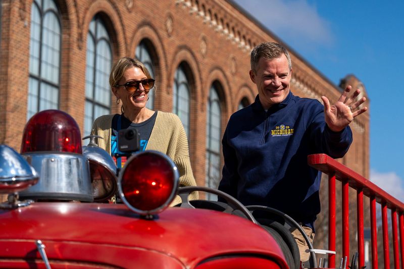 Dusty May, head coach of the University of Michigan men’s basketball team, waves to fans alongside his wife, Anna May, while riding in a parade honoring the team’s NCAA national championship in Ann Arbor on Saturday, April 11, 2026.
