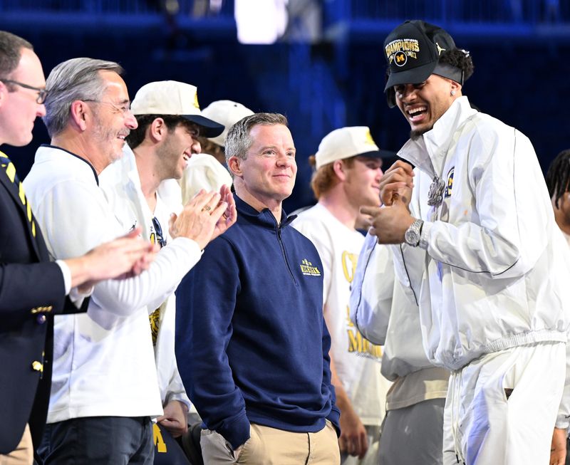 It’s all smiles around Michigan head coach Dusty May, center, after it was announced that May has a new contract, at left is interim Michigan president Domenico Grasso and at right is Michigan forward Yaxel Lendeborg, right, during the celebration for the 2026 Michigan Men’s Basketball National Championship team at Crisler Center on April 11, 2026 in Ann Arbor, Mich.