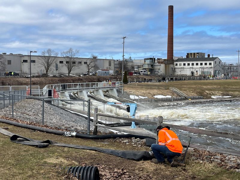 A worker adjusts hoses leading from pumps up river of the Cheboygan Dam on Monday, April 13, 2026, as state and local officials work to mitigate high water levels behind the Cheboygan Lock and Dam Complex.