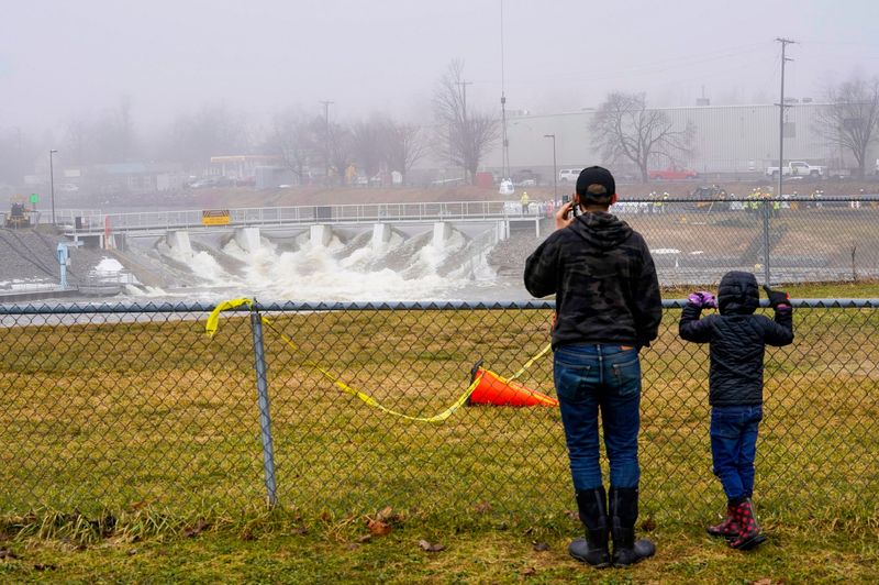 Emerick Passeno, 15, of Indian River, and his sister Peatl Passeno, 7, watch the raging waters on the Cheboygan River rush through the Cheboygan Dam as crews work to reinforce the dam on Tuesday, April 14, 2026.