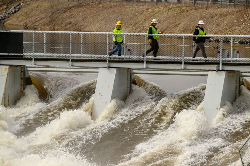 Workers cross as bridge as floodwaters climb towards the top of the Cheboygan dam, April 14, 2026. Recent heavy rains have risen water heights to dangerous levels.