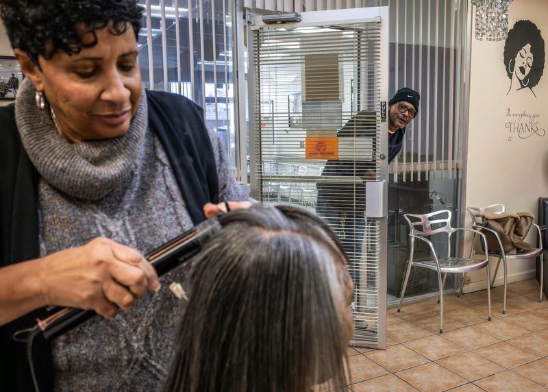 Shep's Barber & Beauty Shop owner Dorothy Grigsby, left, 76, curls a customer's hair as her son, Terrance Harris, 57, leans in the door separating the salon from the barbershop on Thursday, Feb. 5, 2026.