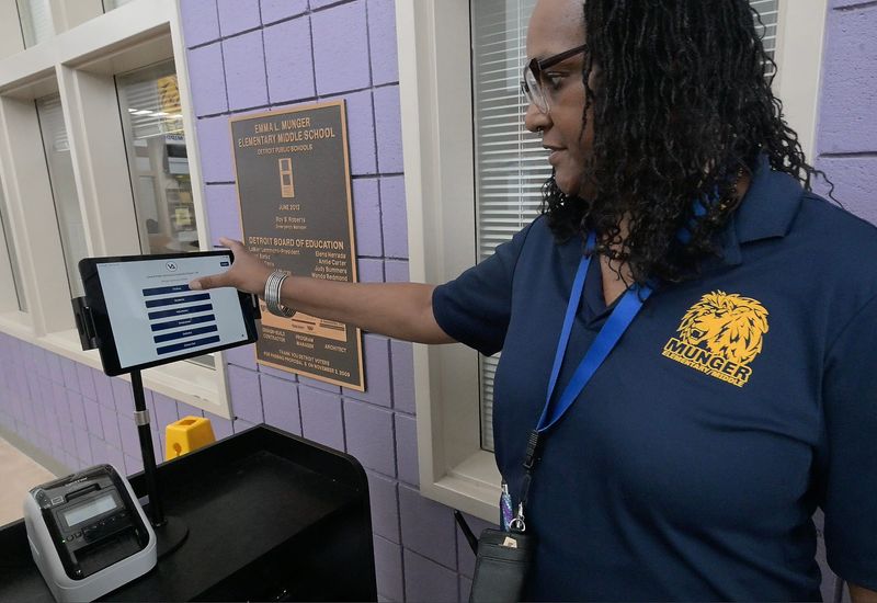 Munger Elementary-Middle School security guard Dawn Miller-Paris demonstrates the process of entering the Detroit public school with various safety measures installed including facial recognition on April 16, 2026. After a person's identity is verified, they walk through scanners and get a bag check if needed. After being buzzed in, security will help set up a school pass.