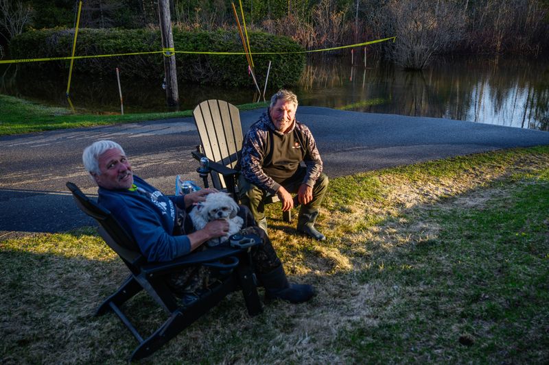Dennis Anderson, 69, left, and Kurt Myers, 70 relax after spending the day piling hundreds of sandbags around their homes on Grace Street along the Sturgeon River to prevent floodwater from breaching them on Thursday, April 16, 2026, in Indian River, Michigan. Katy Kildee / The Detroit News