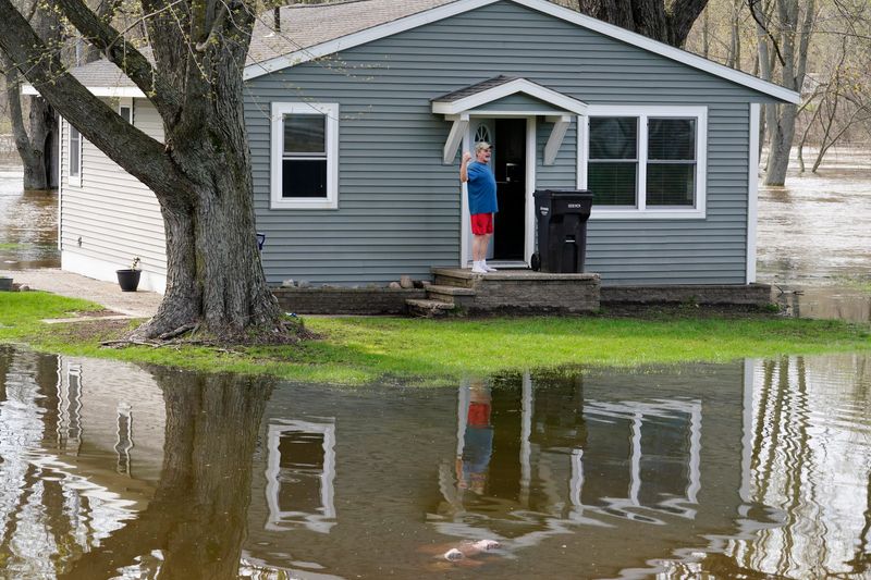 A man yells at his neighbor that he is packing up to leave his flooded home on the Muskegon River in Cedar Creek Township after Michigan State trooper Maxwell Nichols encouraged him to evacuate on Friday, April 17, 2026. Nichols warned that the river was continuing to rise.