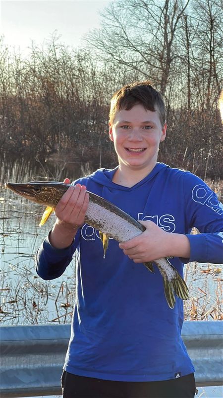 Gavin Bruney holds the northern pike he caught with his bare hands on a flooded road alongside Crooked Lake east of Petoskey in Emmet County on Thursday, April 16, 2026.