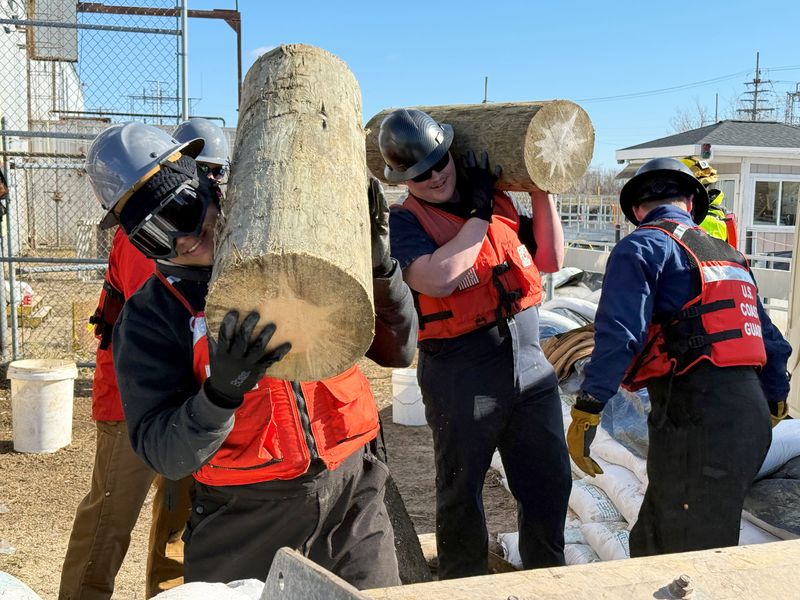 Coast Guardsmen crack jokes as they remove segments of a telephone pole that had floated down the river toward the hydroelectric plant on Monday, April 20, 2026.