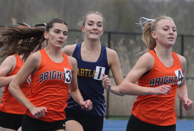 Hartland's Elliana Neuer (1) smiles while running with Brighton's Lydia LaMarra (3) and Ella Lorenz (4) in a 1,600-meter race on Tuesday, April 21, 2026.