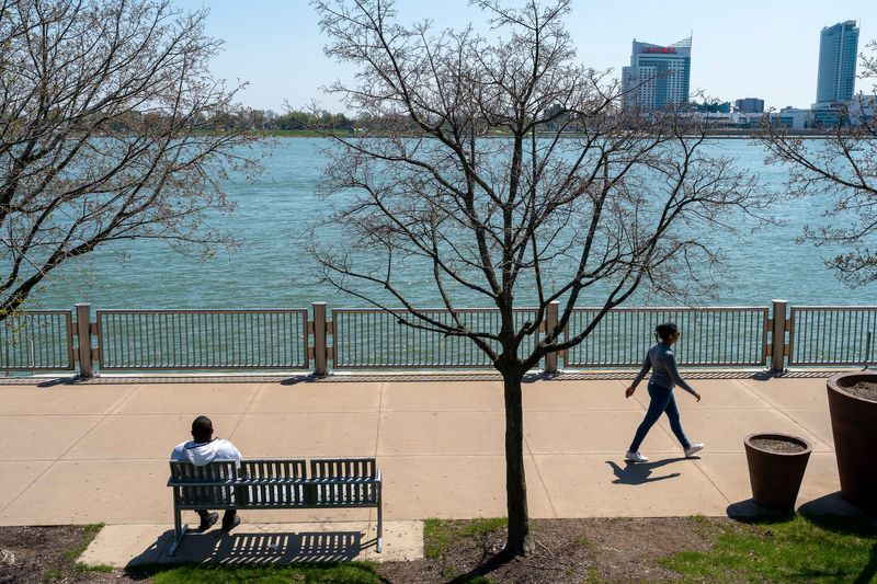 A person sits on a bench as another walks along a reopened section of the Detroit RiverWalk between Beaubien and Rivard streets in Detroit on Thursday, April 23, 2026.