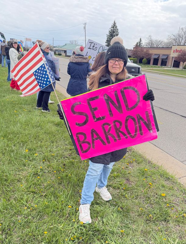 Melody Day holds a sign reading “Send Barron” as she stands along 24th Avenue near Keewahdin Road during a May Day protest on May 1, 2026, in Fort Gratiot Township.