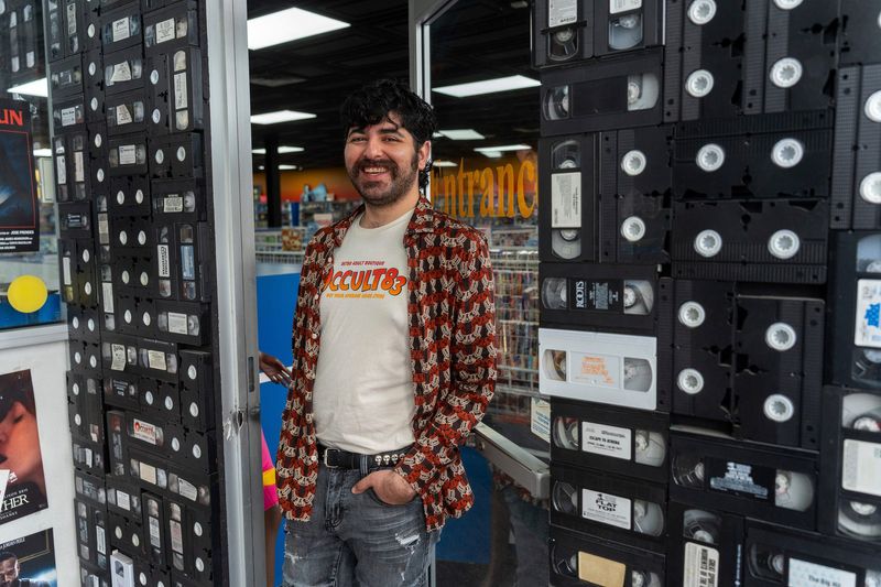 Doran Konja, owner of Occult83, smiles as he stands inside his video store in Dearborn Heights on Thursday, April 16, 2026. The shop has evolved as physical media declines, shifting toward collectibles and niche retail.