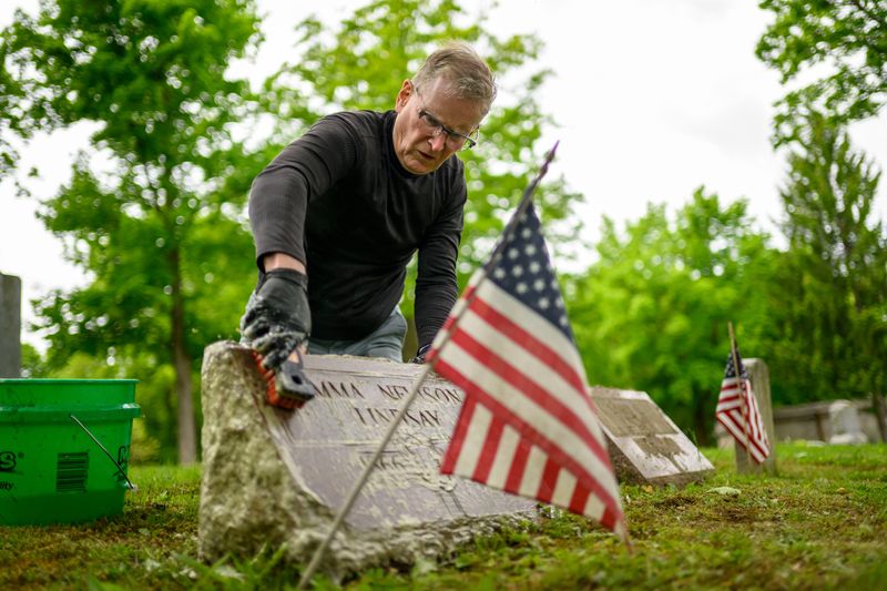 Volunteer Curt Perry, with the Cemetery Renewal Task Force, cleans a tombstone at Rural Hill cemetery in Northville, May 20, 2026, in preparation for Memorial Day.