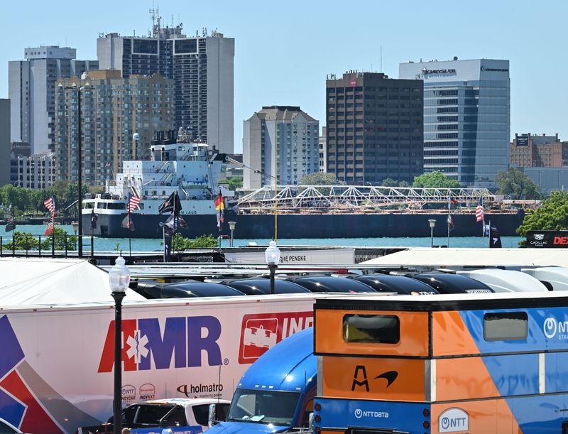 A freighter makes it down the Detroit River past trucks and trailers for the upcoming Detroit Grand Prix on May 28, 2026. The river's crossings to Canada highlight Michigan's status as a supply chain hub that makes retail theft and fraud a particularly crucial issue for the state.