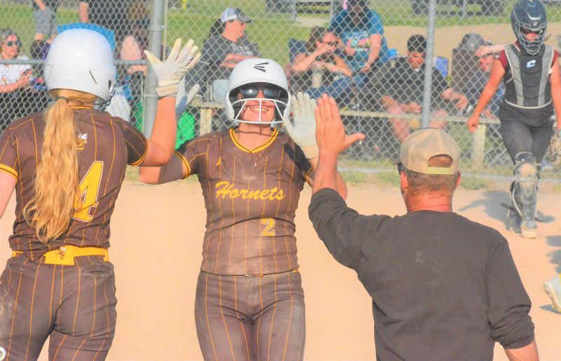Pellston senior Breanna Willis (2) gets a pair of high-fives from senior Ella Klungle (left) and assistant coach Jack Carter after Willis scored a run during an MHSAA Division 4 district softball final against Harbor Light at Pellston on Friday, May 29.