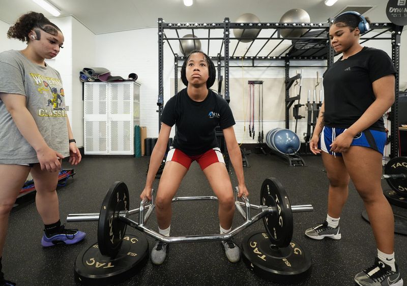 Lansing School District Student Development Program Lansing Eastern sophomore Olivia Sarnpaio, left, and freshman RaniyJah Lewis, right, spot freshman Surae Curtis as she works out, Tuesday, June 2, 2026, in the weight room at Don Johnson Fieldhouse in Lansing. Weight training is one of several activities students can participate in as part of the Lansing School District's Student Development Program.