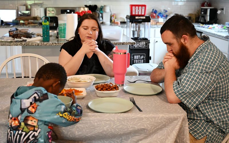 Aly Markwell, 30, prays before dinner with her husband, Chad, right, 27, and one of their sons, soon to be adopted, on June 8, 2026 at the Markwell home in Potterville, Mich.