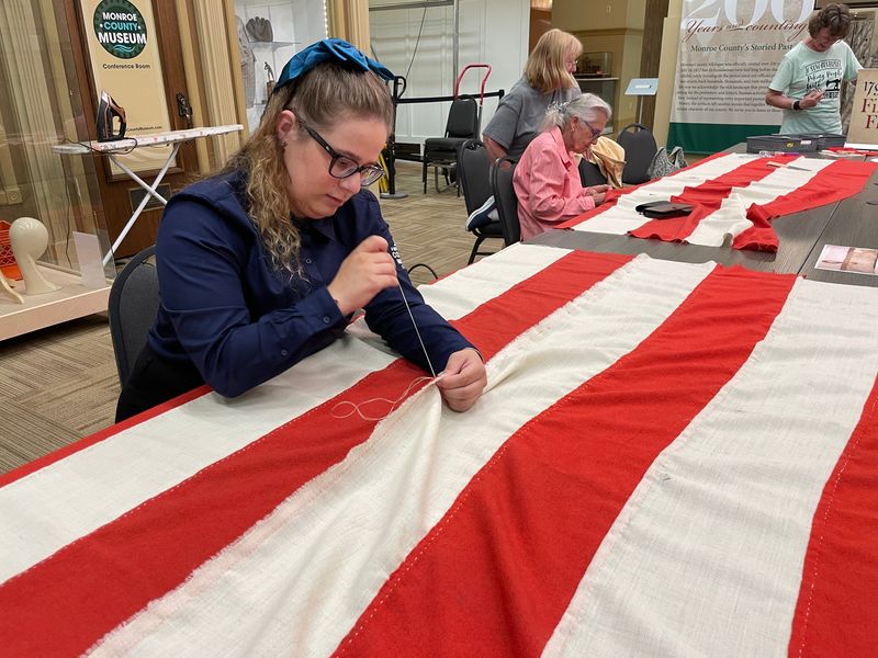 Lily Close, history presenter at the Monroe County Museum, sews some of the flag's 15 stripes together June 14 at the museum.